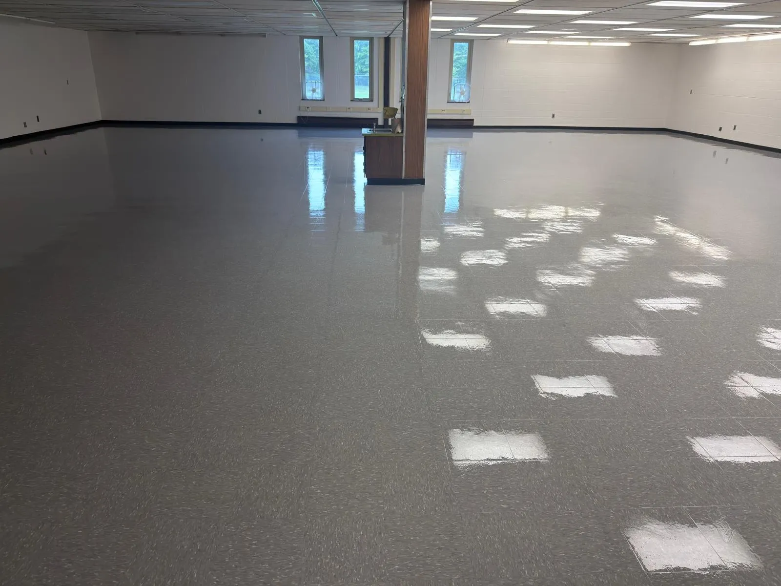 Large room with freshly waxed, high-gloss vinyl tile floor reflecting the ceiling lights
